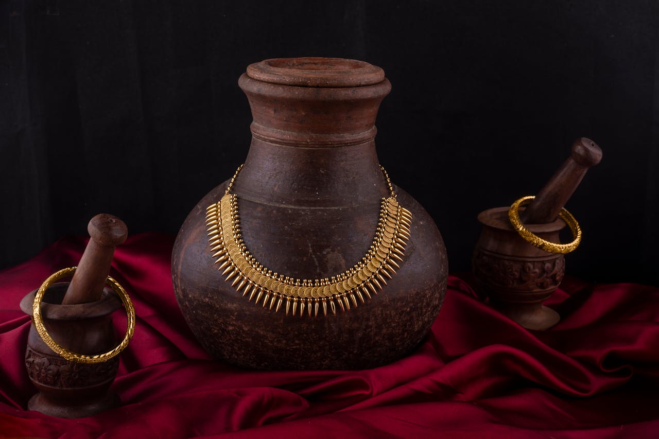 The Art of Drawing Readers In: Your attractive post title goes here Elegant still life of traditional Indian necklace and bangles on vintage pottery with red fabric backdrop.